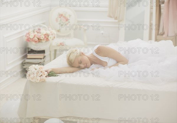 Bride sleeping on bed with bouquet of flowers