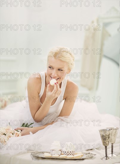 Smiling bride eating cupcakes on bed