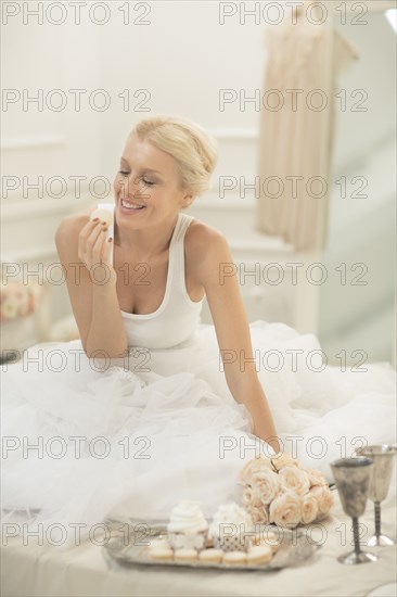 Smiling bride eating cupcakes on bed