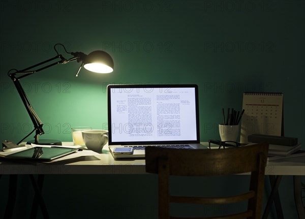 Computer and cell phone illuminated by desk lamp at night