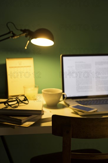 Computer and cell phone illuminated by desk lamp at night