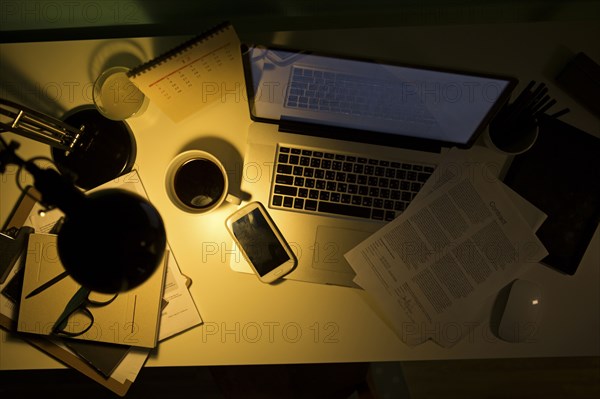 Computer and cell phone illuminated by desk lamp at night