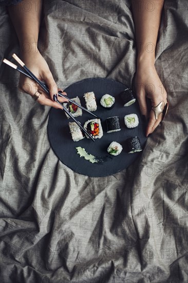 Woman eating sushi with chopsticks in bed