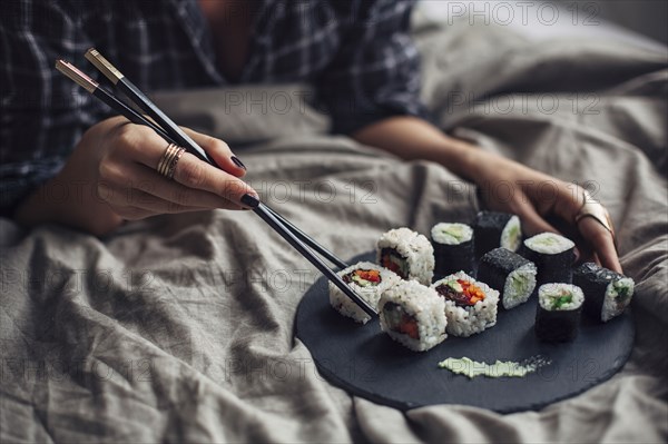 Woman eating sushi with chopsticks in bed