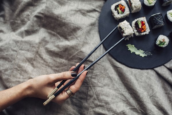 Hand of woman reaching for platter of sushi on bed