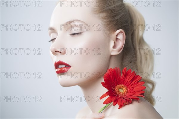 Caucasian woman with red lipstick holding matching flower