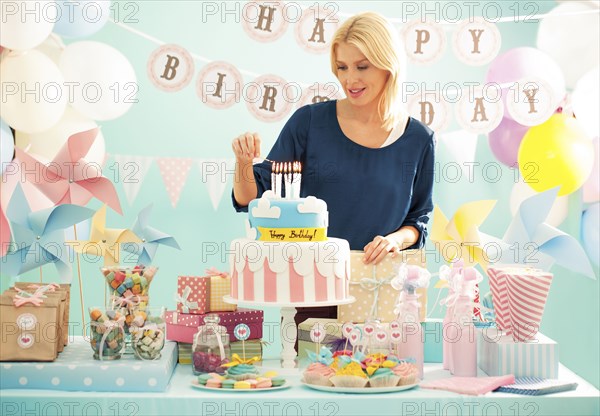 Woman lighting candles on birthday cake at party