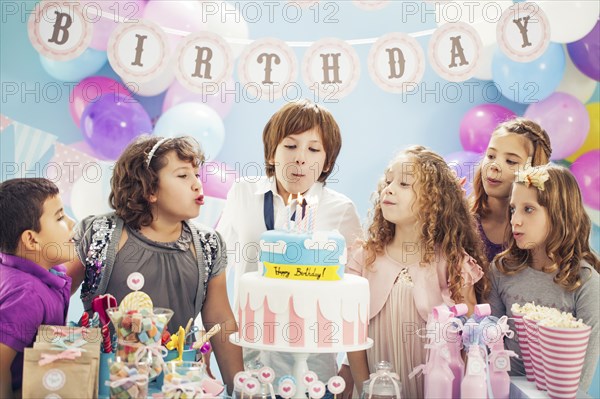 Boy blowing out candles on birthday cake at party