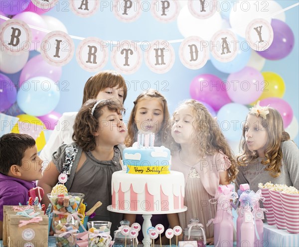Children blowing out candles on birthday cake in party