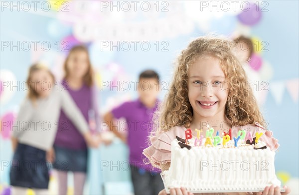 Smiling girl holding birthday cake at party