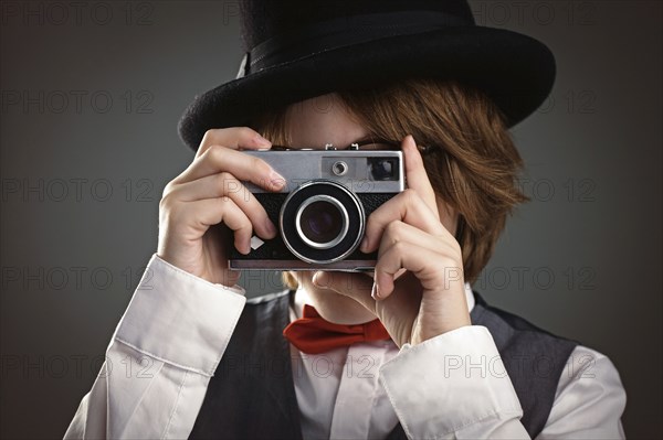 Close up of boy in top hat photographing with vintage camera