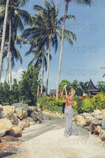 Caucasian woman photographing palm trees on beach