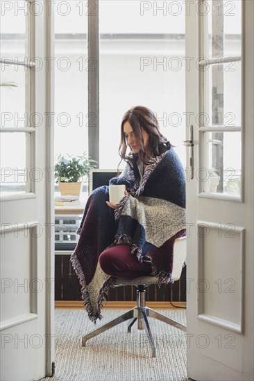 Caucasian woman in blanket drinking cup of coffee