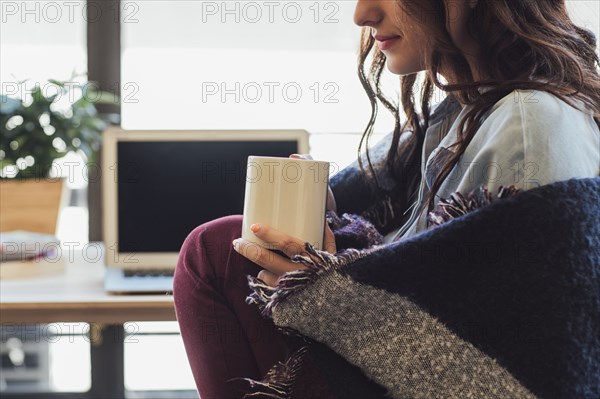 Caucasian woman in blanket drinking cup of coffee