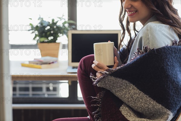 Caucasian woman in blanket drinking cup of coffee