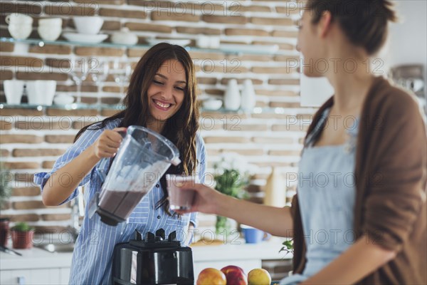 Caucasian women pouring smoothie in kitchen