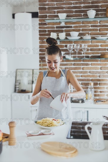 Caucasian woman pouring sauce on pasta in kitchen