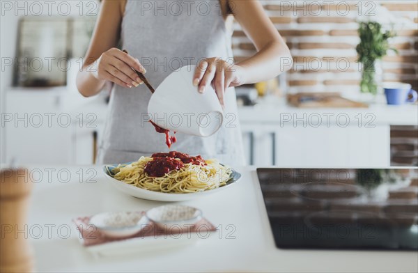 Caucasian woman pouring sauce on pasta in kitchen