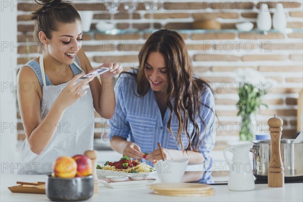 Caucasian women photographing pasta in kitchen