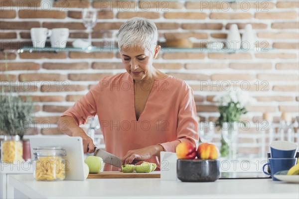 Older Caucasian woman cutting apples in kitchen