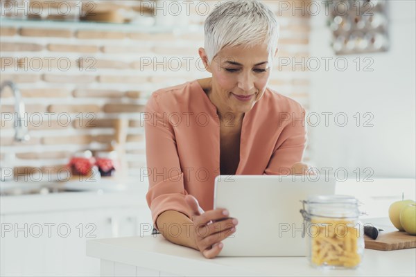 Older Caucasian woman using digital tablet in kitchen