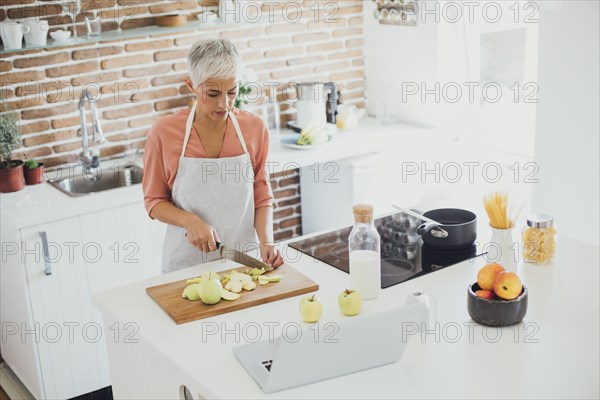 Older Caucasian woman cutting apples in kitchen