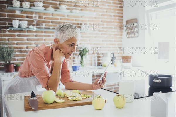 Older Caucasian woman using digital tablet in kitchen