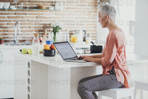 Older Caucasian woman using laptop in kitchen