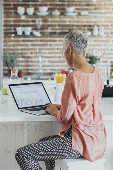 Older Caucasian woman using laptop in kitchen