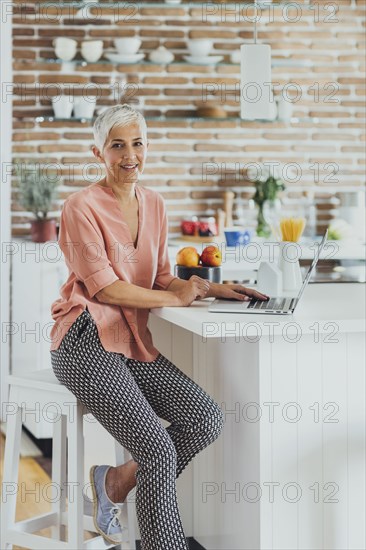 Older Caucasian woman using laptop in kitchen