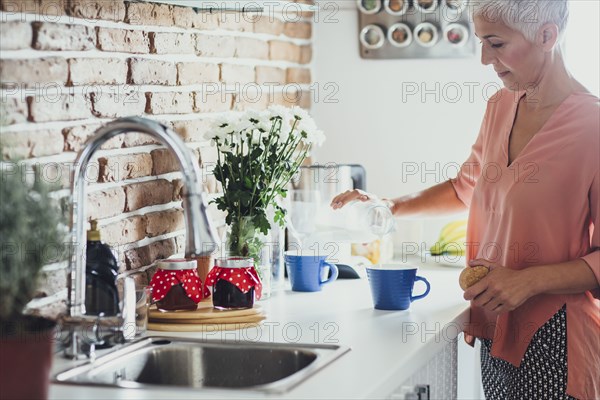Older Caucasian woman making coffee in kitchen