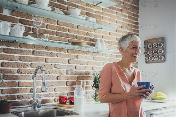 Older Caucasian woman having coffee in kitchen