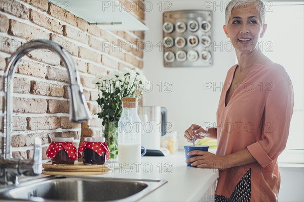 Older Caucasian woman stirring coffee in kitchen