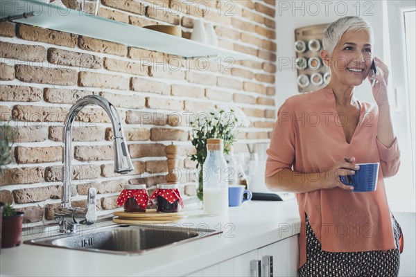 Older Caucasian woman talking on cell phone in kitchen