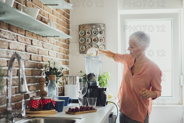 Older Caucasian woman making smoothie in kitchen