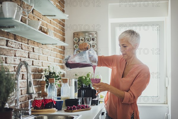 Older Caucasian woman pouring smoothie in kitchen