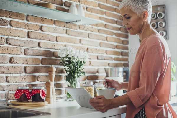 Older Caucasian woman using digital tablet in kitchen