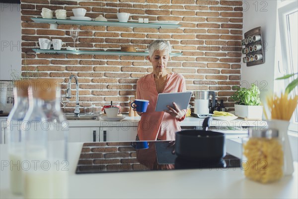 Older Caucasian woman using digital tablet in kitchen