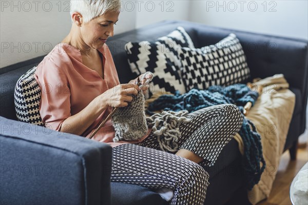 Older Caucasian woman knitting on sofa