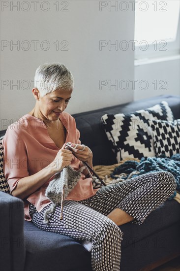 Older Caucasian woman knitting on sofa