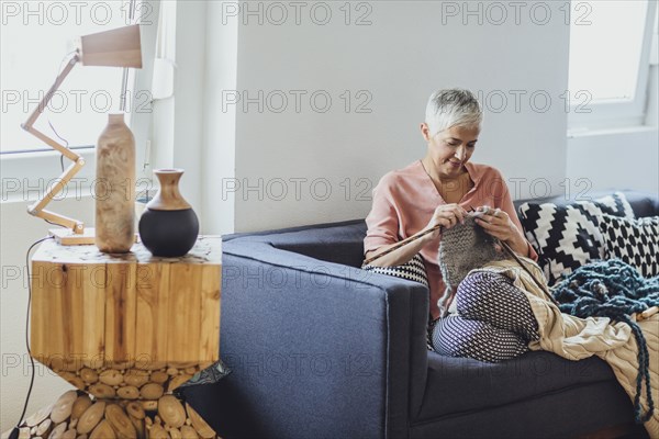 Older Caucasian woman knitting on sofa