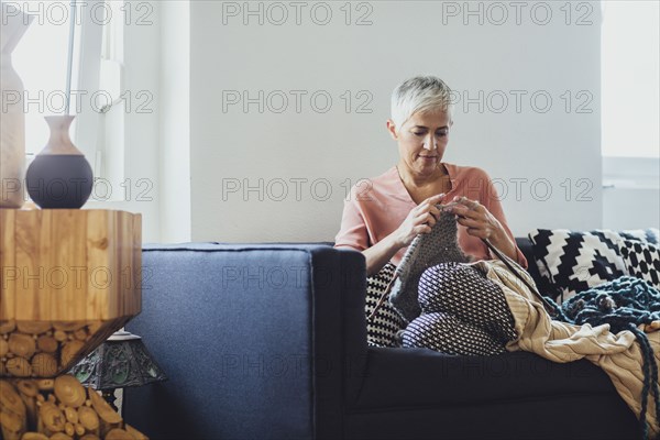 Older Caucasian woman knitting on sofa