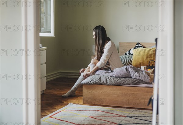 Caucasian woman pulling up sock on bed