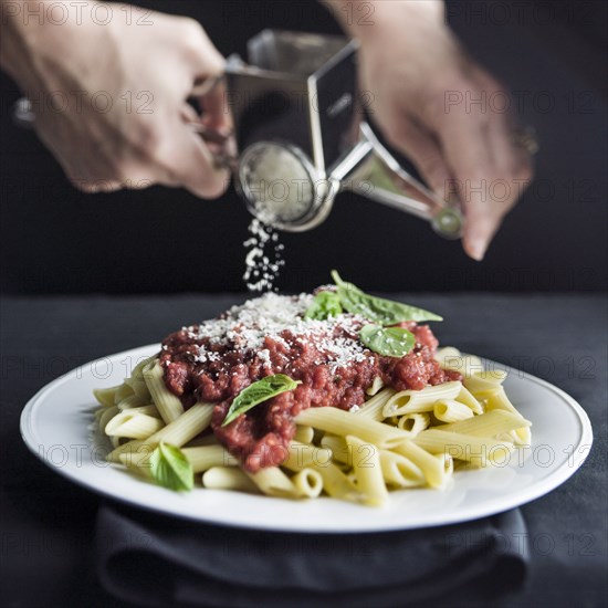 Hands grating parmesan cheese on penne pasta