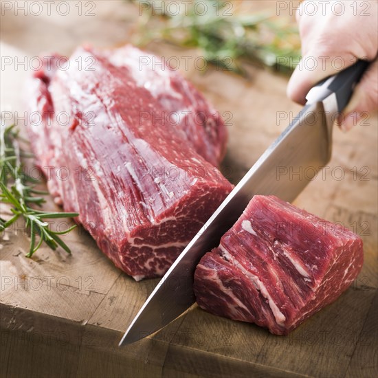 Knife cutting beef tenderloin on wooden table