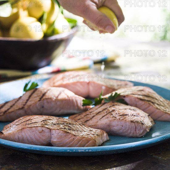 Hand squeezing juice from lemon onto plate of salmon