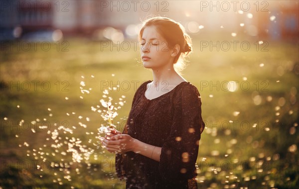 Caucasian woman standing in field with blowing dandelion seeds