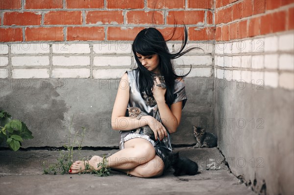 Caucasian woman sitting on sidewalk with cats