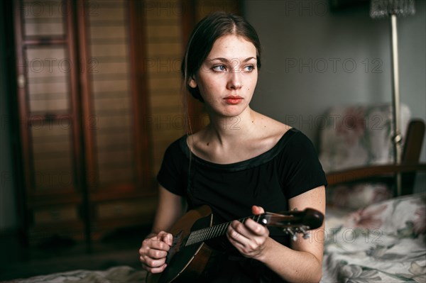 Caucasian woman playing ukulele in bedroom