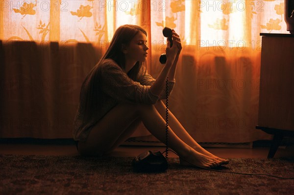 Caucasian woman sitting on floor staring at telephone